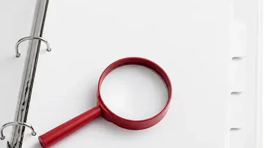 An open ring binder with tabbed dividers beside a magnifying glass